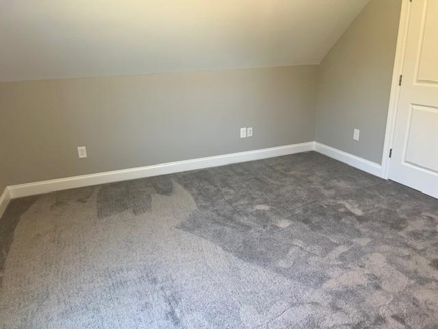 additional living space featuring vaulted ceiling and dark colored carpet