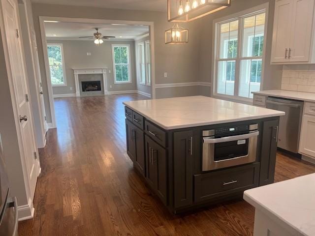 kitchen with dark wood-type flooring, hanging light fixtures, a kitchen island, stainless steel appliances, and white cabinets