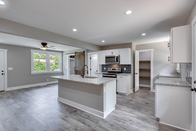 kitchen with tasteful backsplash, a barn door, white cabinets, stainless steel appliances, and a sink