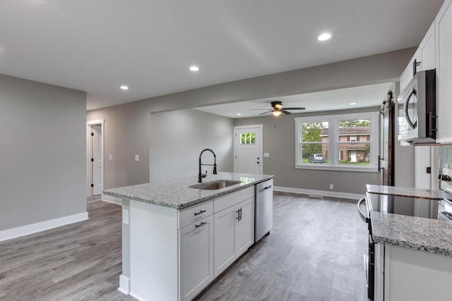 kitchen featuring appliances with stainless steel finishes, a sink, light wood finished floors, and baseboards