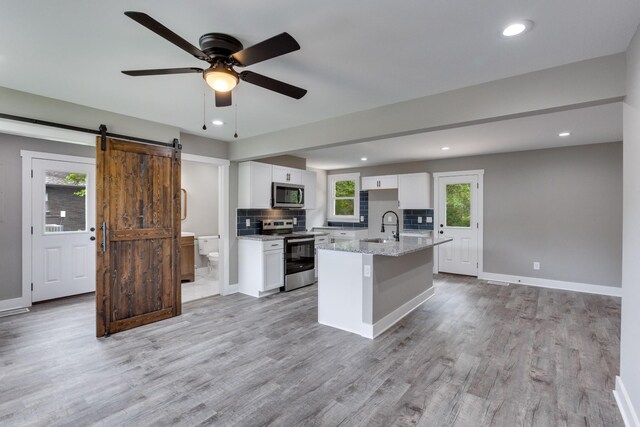 kitchen featuring stainless steel appliances, backsplash, a barn door, white cabinetry, and ceiling fan