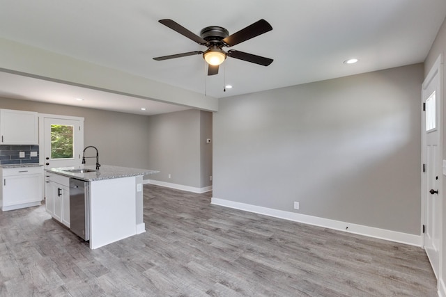 kitchen featuring light wood-style flooring, stainless steel dishwasher, white cabinets, a sink, and baseboards