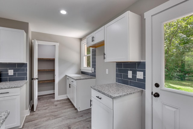 kitchen featuring light stone counters, light wood-type flooring, white cabinets, and decorative backsplash