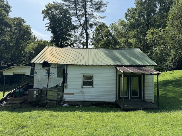 rear view of house with cooling unit, metal roof, and a lawn