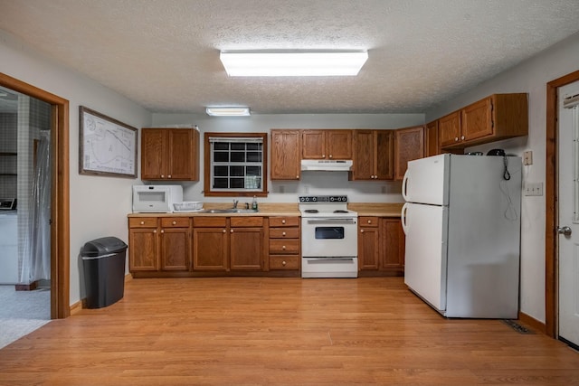 kitchen featuring white appliances, light wood-style floors, brown cabinets, under cabinet range hood, and a sink