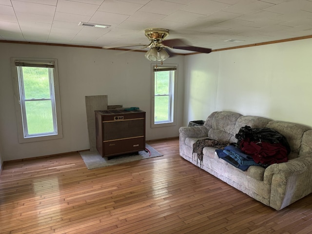 living room featuring wood-type flooring, visible vents, a ceiling fan, and ornamental molding