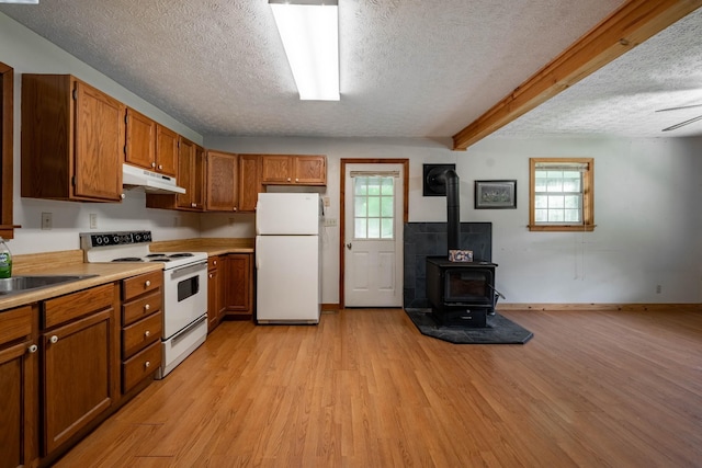 kitchen featuring white appliances, light wood-style floors, brown cabinets, a wood stove, and under cabinet range hood