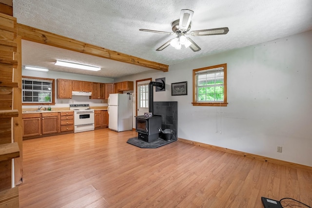 kitchen featuring white appliances, a wood stove, light countertops, a textured ceiling, and light wood-style floors