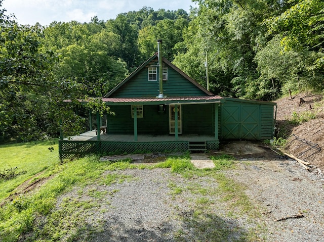 view of front of house with metal roof, driveway, a porch, and a wooded view