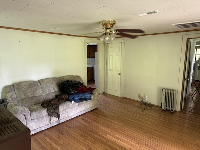 living room featuring radiator, wood-type flooring, visible vents, and ornamental molding