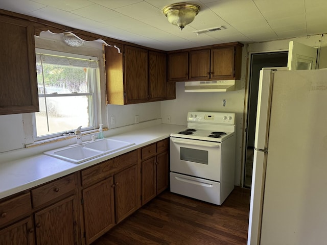 kitchen with under cabinet range hood, white appliances, a sink, visible vents, and dark wood-style floors