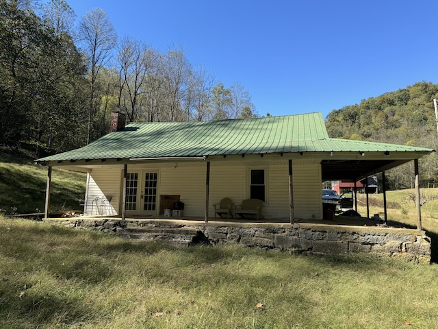 rear view of property with a carport, french doors, metal roof, and a chimney