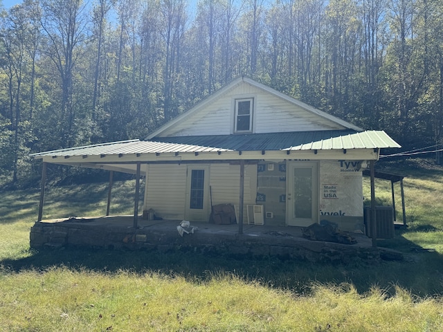 view of front of house featuring a forest view, central AC unit, metal roof, and a patio