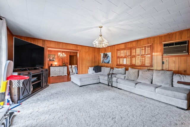 carpeted living room with an AC wall unit, wood walls, and an inviting chandelier