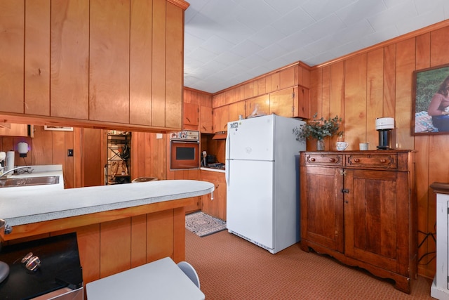 kitchen with a sink, brown cabinetry, light countertops, and freestanding refrigerator