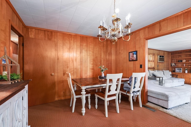 dining room with a notable chandelier, crown molding, wood walls, and light colored carpet