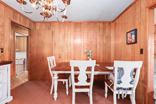 dining room featuring wood walls, carpet, crown molding, and a chandelier