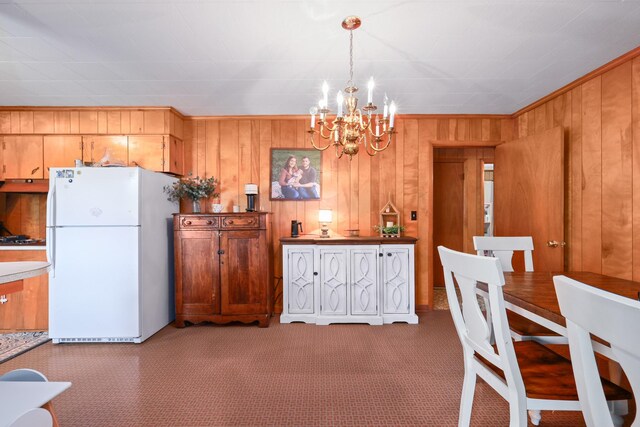 carpeted dining room featuring wooden walls and a chandelier