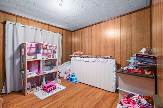 bedroom with crown molding, wooden walls, and wood finished floors