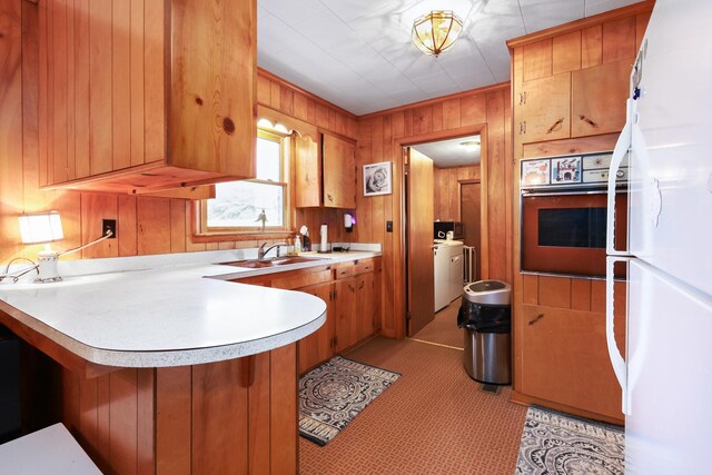 kitchen featuring white refrigerator, wooden walls, oven, sink, and kitchen peninsula