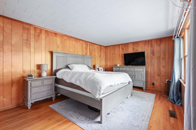 bedroom with light wood-type flooring, wooden walls, and visible vents