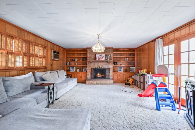 living room with a fireplace, built in features, carpet flooring, wood walls, and an AC wall unit