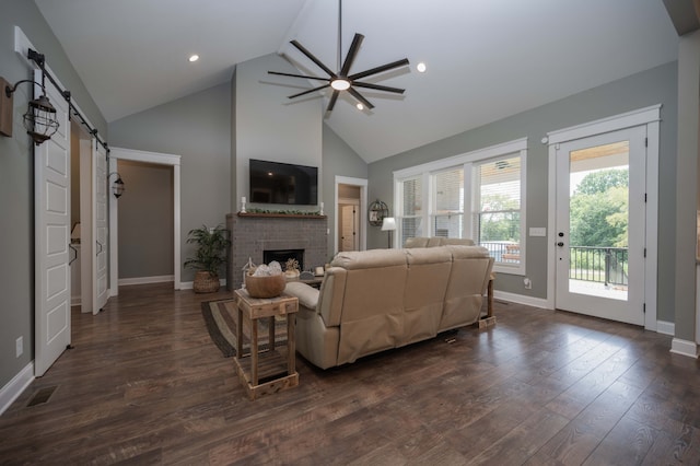 living room featuring ceiling fan, dark wood-type flooring, a barn door, high vaulted ceiling, and a fireplace