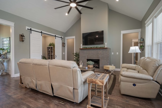 living room with high vaulted ceiling, a brick fireplace, dark hardwood / wood-style floors, a barn door, and ceiling fan