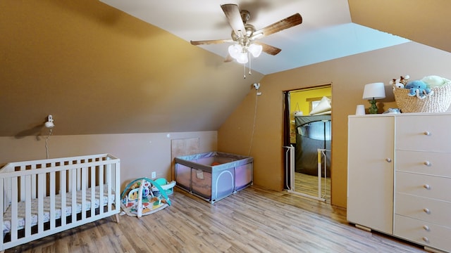 bedroom featuring lofted ceiling, a nursery area, light wood-type flooring, and ceiling fan