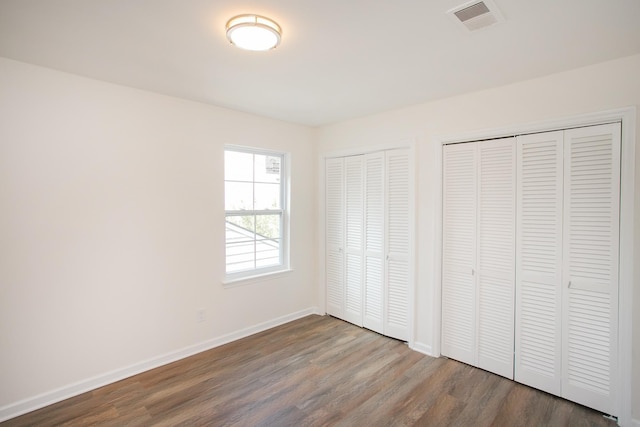 unfurnished bedroom featuring wood-type flooring and two closets