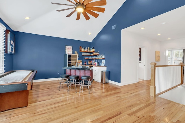 bar with ceiling fan, high vaulted ceiling, and light hardwood / wood-style floors