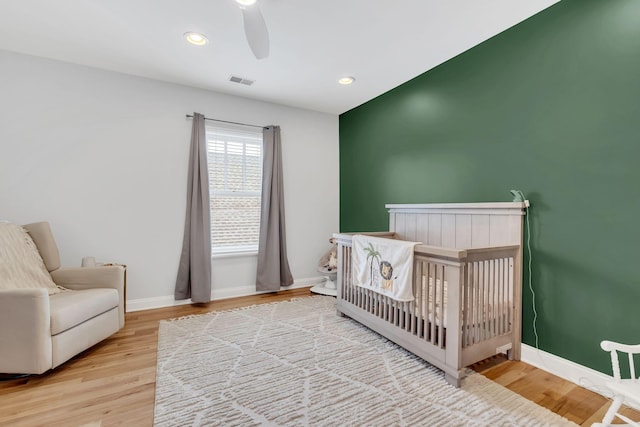 bedroom featuring a crib, ceiling fan, and light wood-type flooring