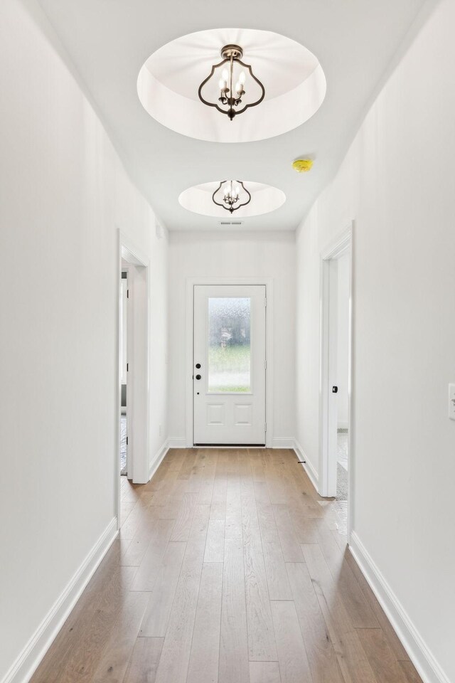 doorway to outside featuring an inviting chandelier, a raised ceiling, and hardwood / wood-style floors