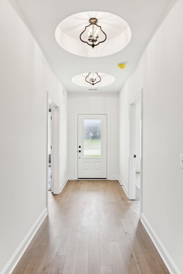 doorway featuring wood finished floors, a raised ceiling, baseboards, and an inviting chandelier