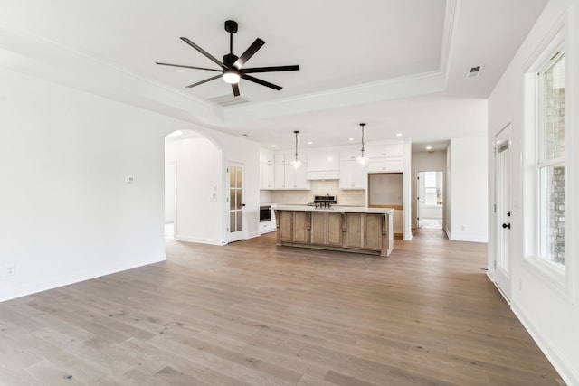 unfurnished living room featuring light hardwood / wood-style flooring, ceiling fan, crown molding, and a tray ceiling