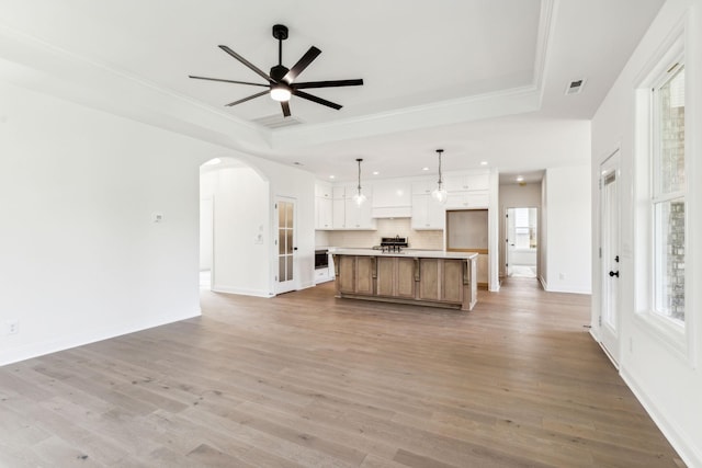 unfurnished living room with light wood-style flooring, arched walkways, a raised ceiling, and a ceiling fan