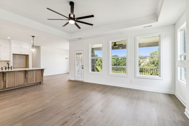 unfurnished living room featuring sink, crown molding, light wood-type flooring, ceiling fan, and a raised ceiling