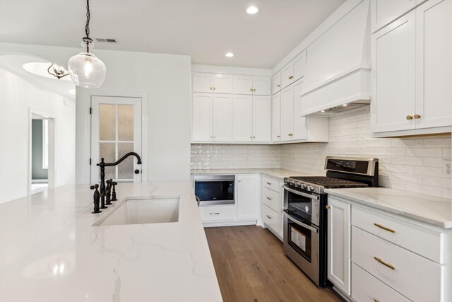 kitchen featuring stainless steel appliances, sink, light stone countertops, hardwood / wood-style flooring, and custom range hood