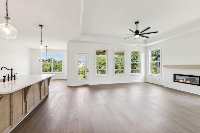 unfurnished living room featuring a tray ceiling, dark wood-style flooring, and a glass covered fireplace