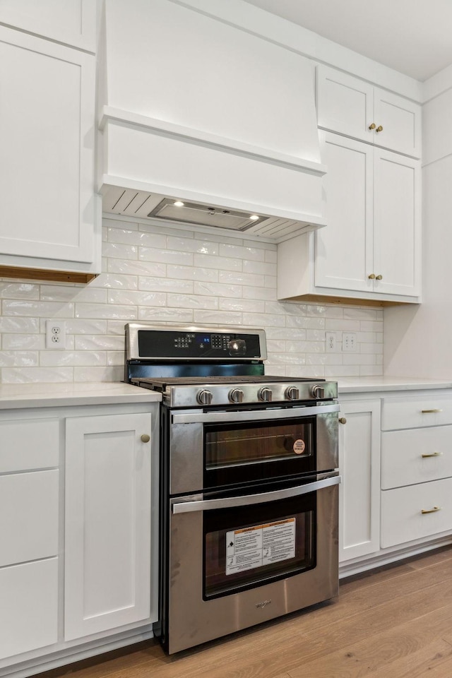 kitchen featuring double oven range, white cabinetry, tasteful backsplash, and premium range hood