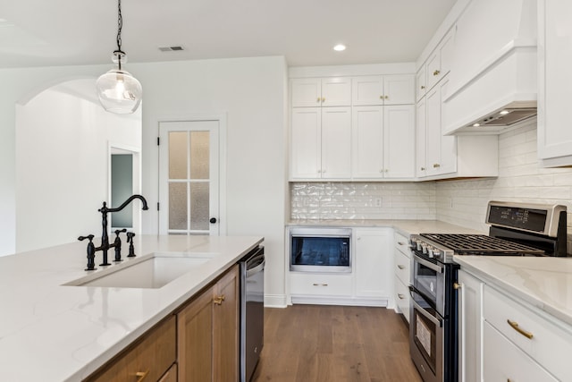 kitchen with appliances with stainless steel finishes, wood-type flooring, white cabinets, and custom range hood