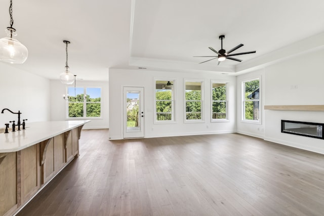 unfurnished living room with hardwood / wood-style flooring, a raised ceiling, and ceiling fan