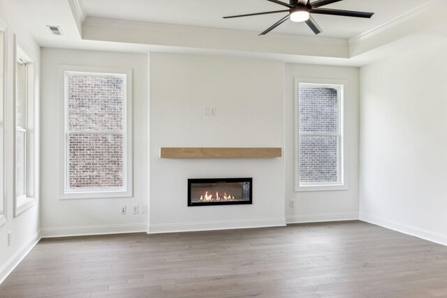 unfurnished living room featuring plenty of natural light, ceiling fan, hardwood / wood-style flooring, and a raised ceiling