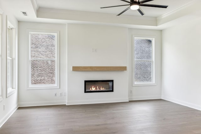 unfurnished living room featuring ornamental molding, wood finished floors, a raised ceiling, and visible vents