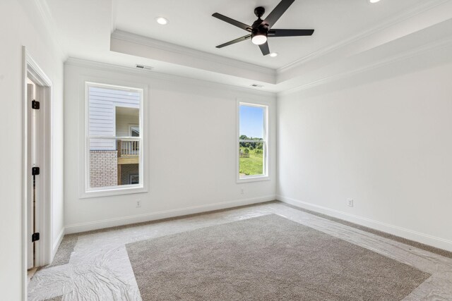 empty room featuring ceiling fan, a raised ceiling, light colored carpet, and ornamental molding