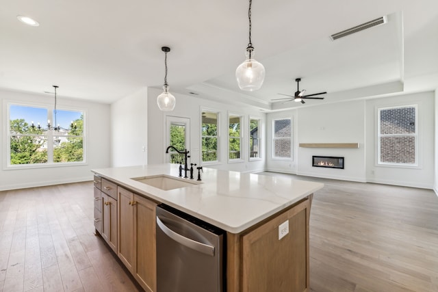 kitchen with light wood-type flooring, dishwasher, sink, a raised ceiling, and a center island with sink