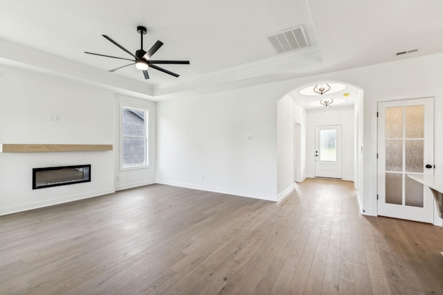 unfurnished living room with arched walkways, a raised ceiling, visible vents, wood-type flooring, and baseboards