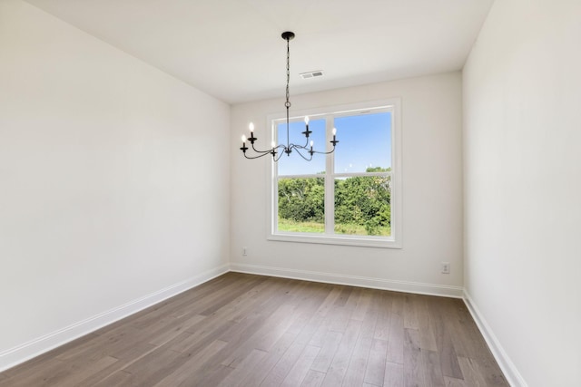 unfurnished dining area featuring an inviting chandelier, visible vents, baseboards, and wood finished floors