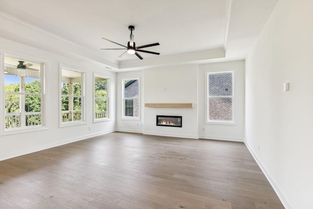 unfurnished living room with a glass covered fireplace, a raised ceiling, ceiling fan, and hardwood / wood-style flooring