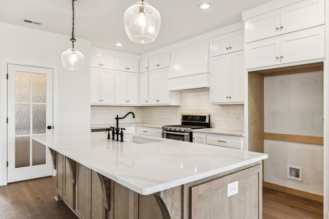 kitchen featuring dark hardwood / wood-style floors, premium range hood, stainless steel range oven, and an island with sink